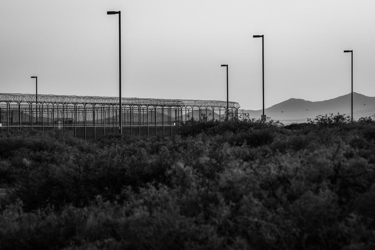 Tall fences with barbed wire are seen with mountains in the distance.