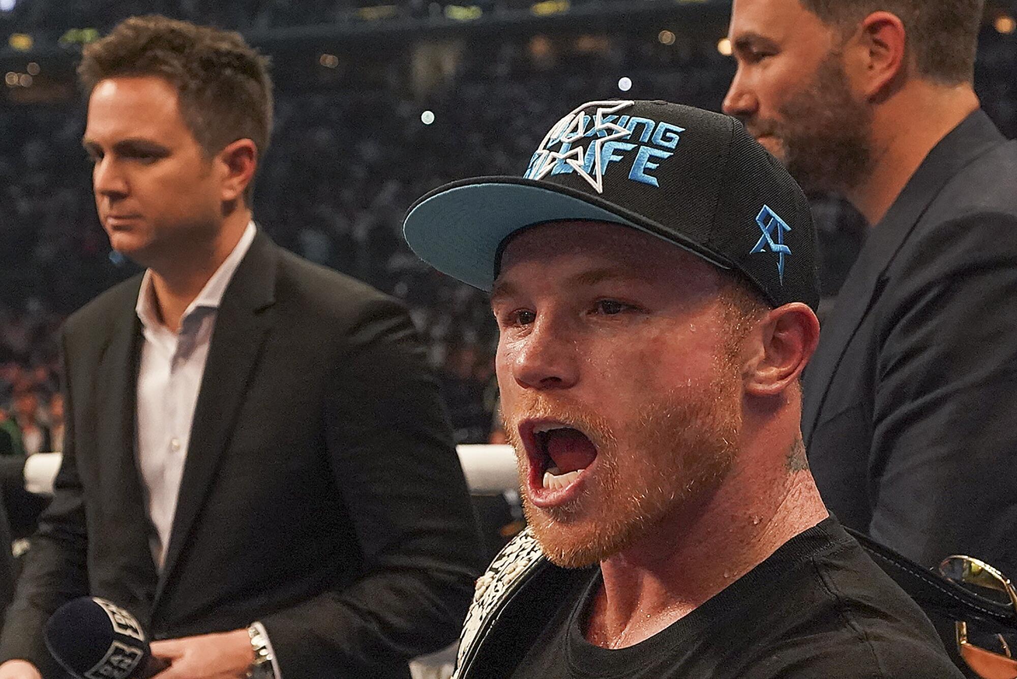 Canelo Álvarez, dressed in a black T-shirt and hat, with his mouth open