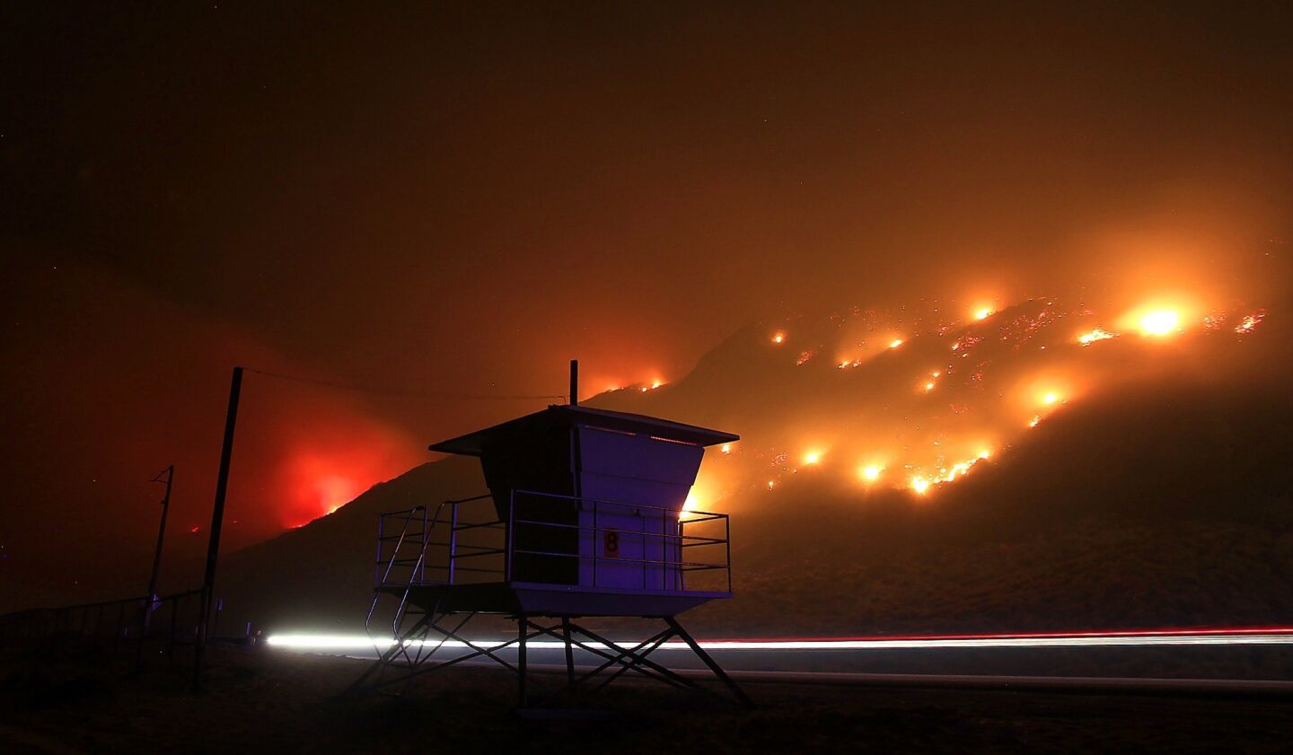 A car passes a lifeguard tower on Pacific Coast Highway as flames head toward the ocean south of Oxnard.