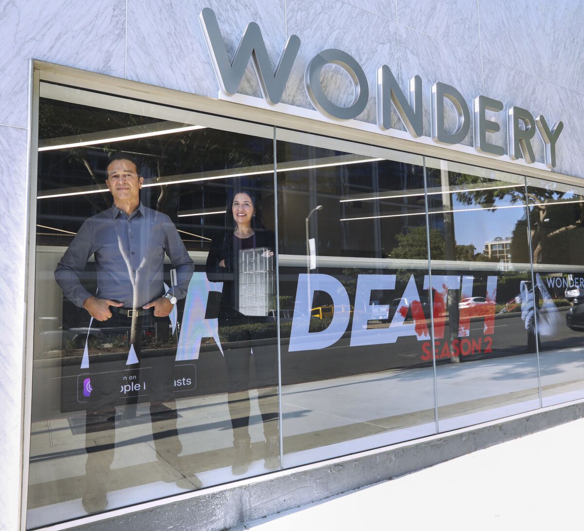 Hernan Lopez and Jen Sargent behind a display window of a building with Wondery above the window on the outside.