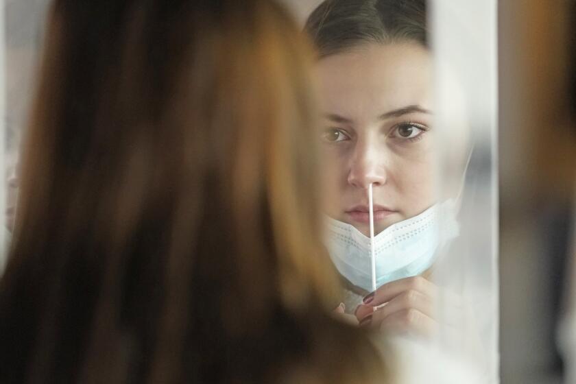 FILE — In this Nov. 18, 2020, file photo, University of Utah student Abigail Shull takes a rapid COVID-19 test in Salt Lake City. As coronavirus cases are surging around the U.S., some colleges and universities are rethinking some of their plans for next semester. (AP Photo/Rick Bowmer, File)