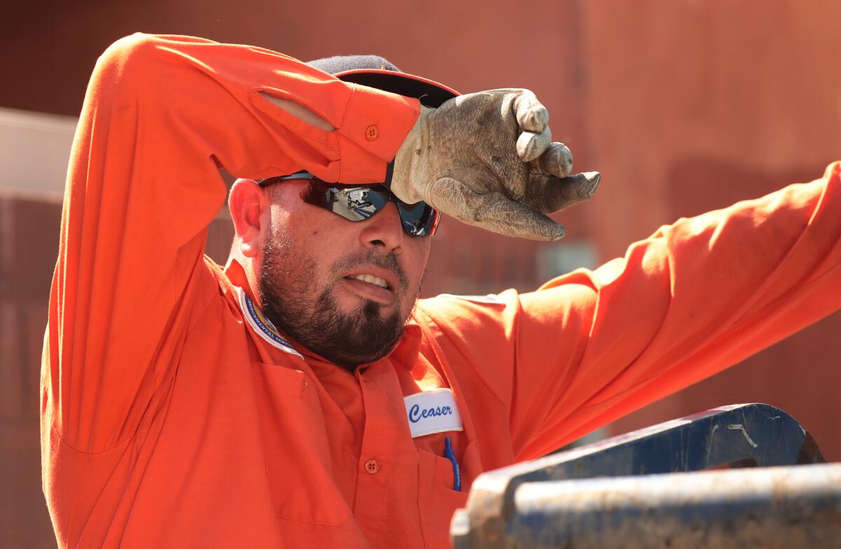 Ceaser Trejo wipes his forehead as he works through the heat wave loading large trash bins into the sanitation truck.