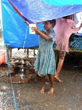 A girl collects rain water running off of her tent at a camp for people displaced by a cyclone near Labutta, Myanmar.
