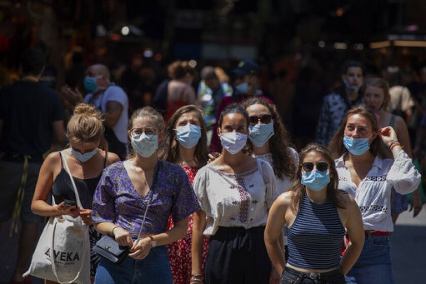 Tourists wearing face masks wait to cross a road in downtown Barcelona, Spain, Thursday, July 16, 2020. With Europe's summer vacation season kicking into high gear for millions weary of months of lockdown, scenes of drunken British and German tourists on Spain's Mallorca island ignoring social distancing rules and reports of American visitors flouting quarantine measures in Ireland are raising fears of a resurgence of infections in countries that have battled for months to flatten the COVID-19 curve. (AP Photo/Emilio Morenatti)