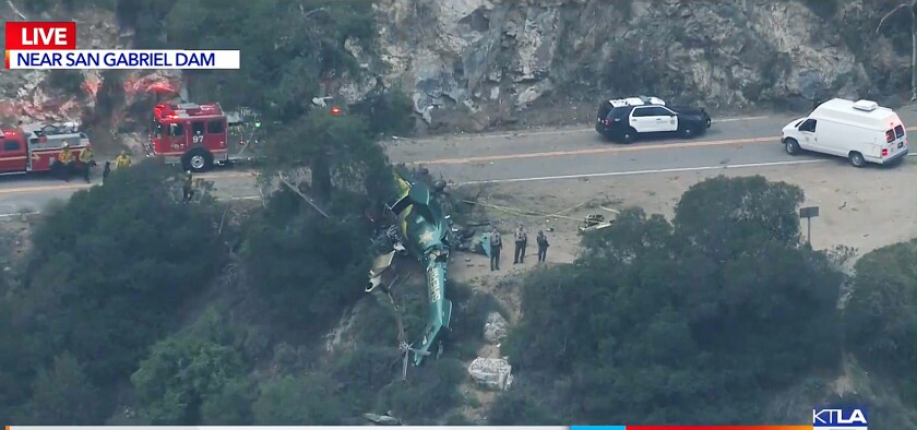 A green helicopter lies on its side after crashing near a road