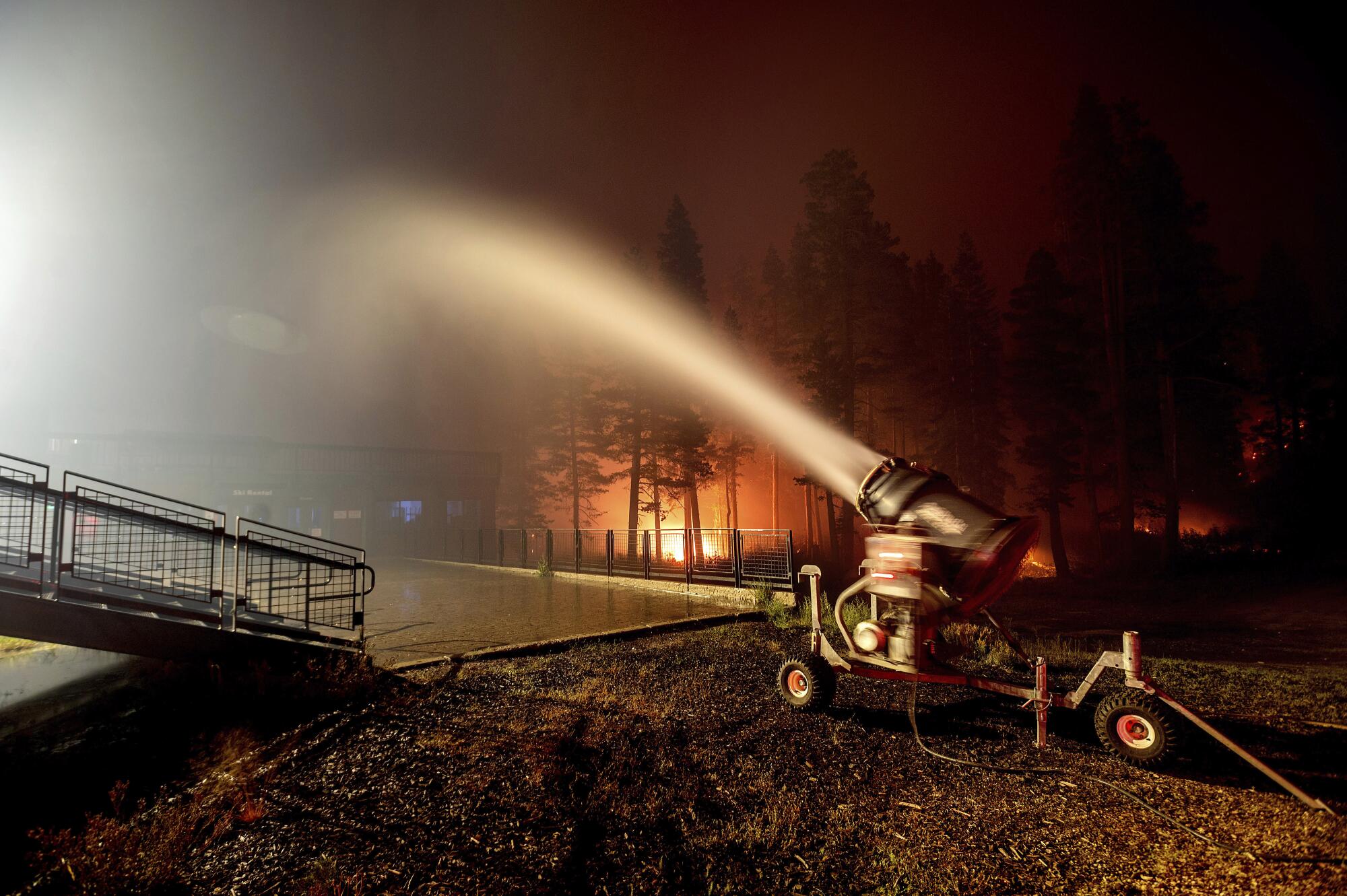 A fountain of water emerges from a snowmaking machine, with flames in the background.