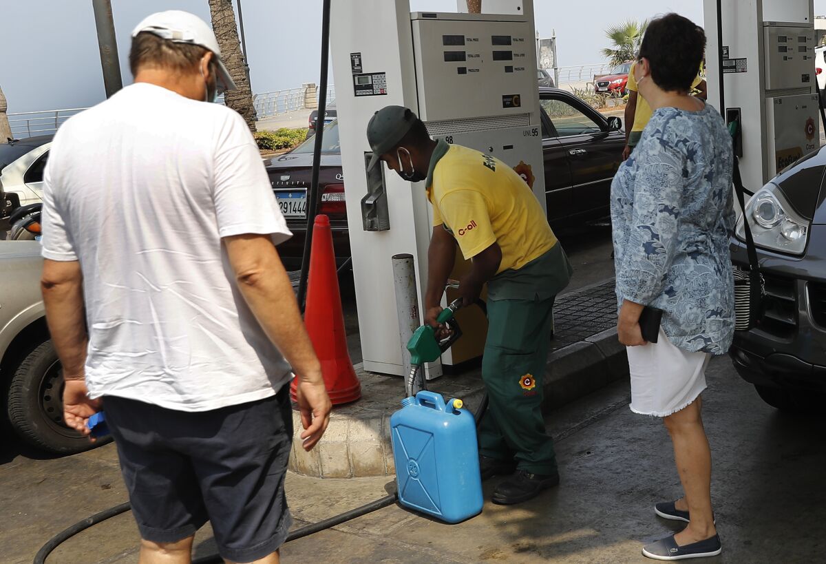 Lebanese citizens look at a gas station worker, center, fills gasoline on their jerry can to power their home generator while the power remains shut off about 20 hours a day, in Beirut, Lebanon, Wednesday, July 29, 2020. Lebanon is hurtling toward a tipping point at an alarming speed, driven by financial ruin, collapsing institutions, hyperinflation and rapidly rising poverty _ with a pandemic on top of that. The collapse threatens to break a nation seen as a model of diversity and resilience in the Arab world. (AP Photo/Hussein Malla)