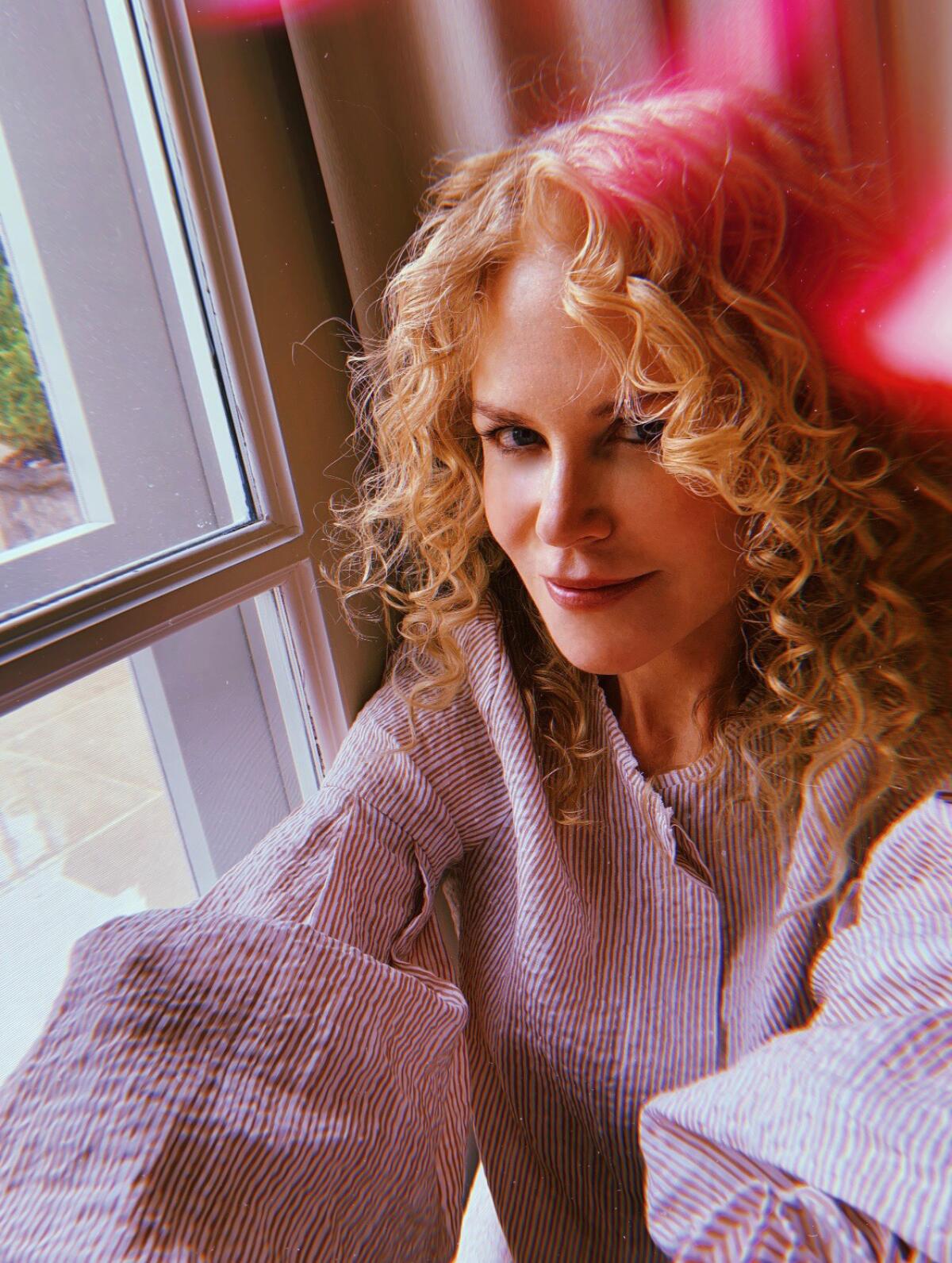 A woman with curly hair sits at a window