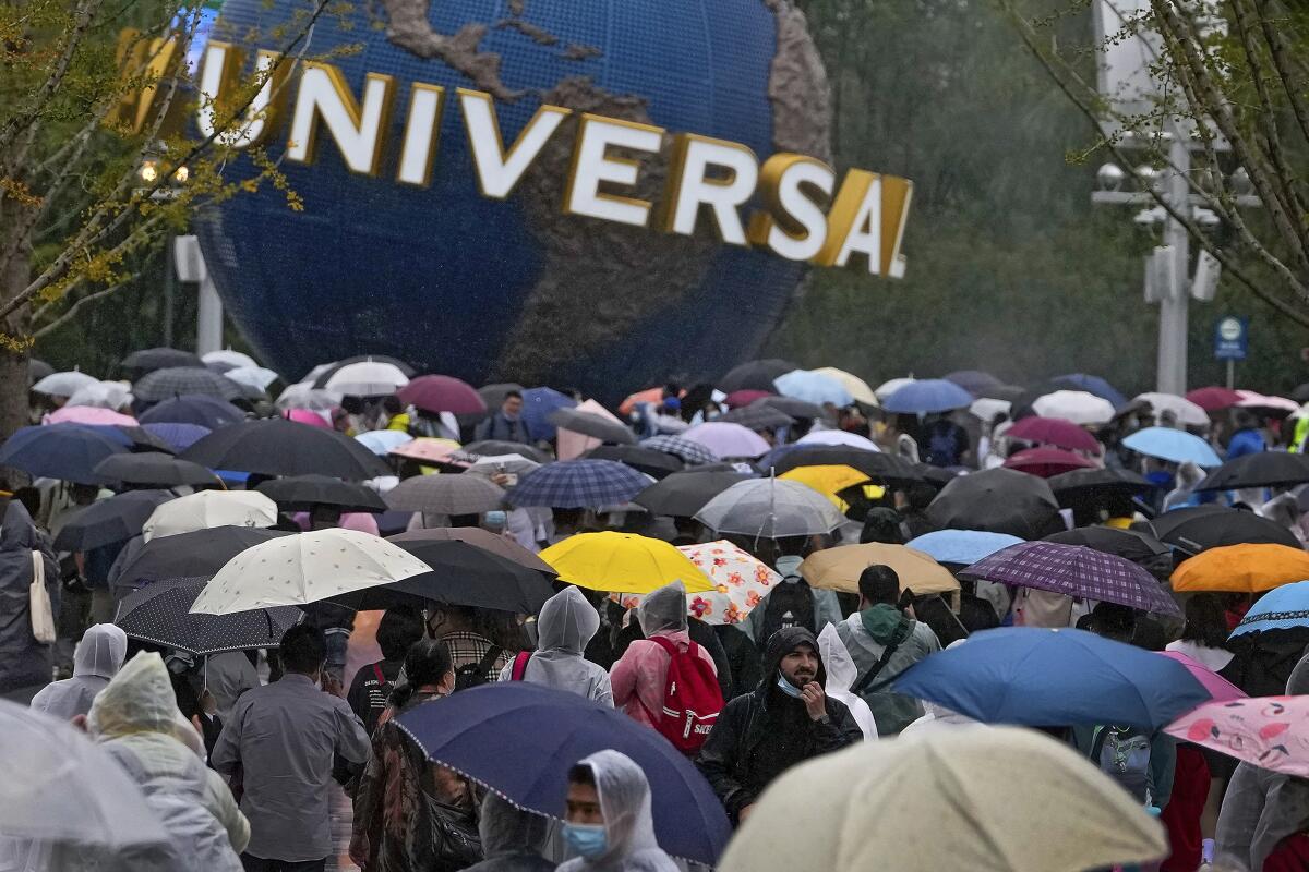 Personas con impermeables y paraguas caminan por una plaza cerca de la entrada de Universal Studios Beijing en Beijing 