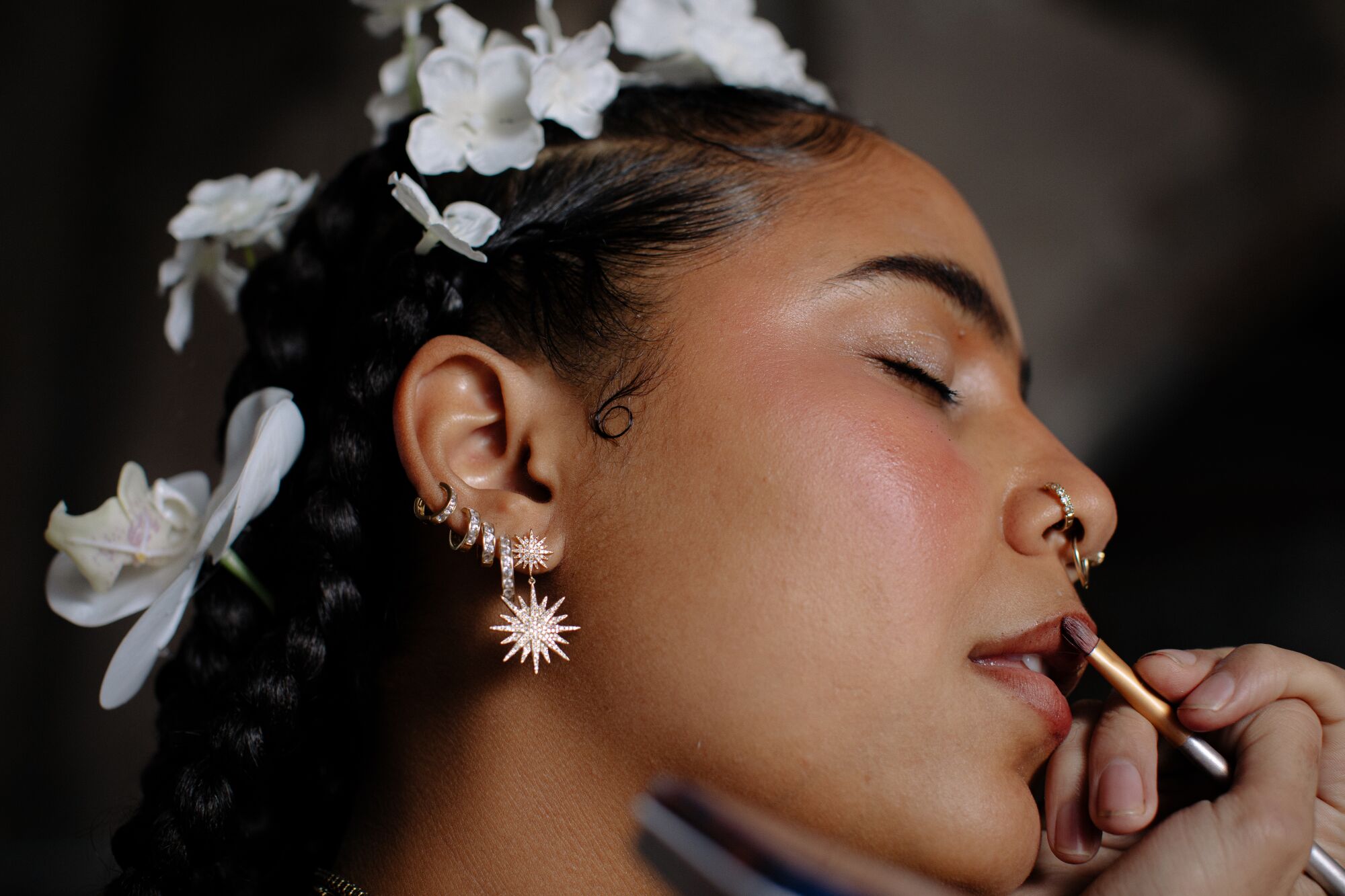 A close-up of a woman with her eyes closed and white flowers in her hair.