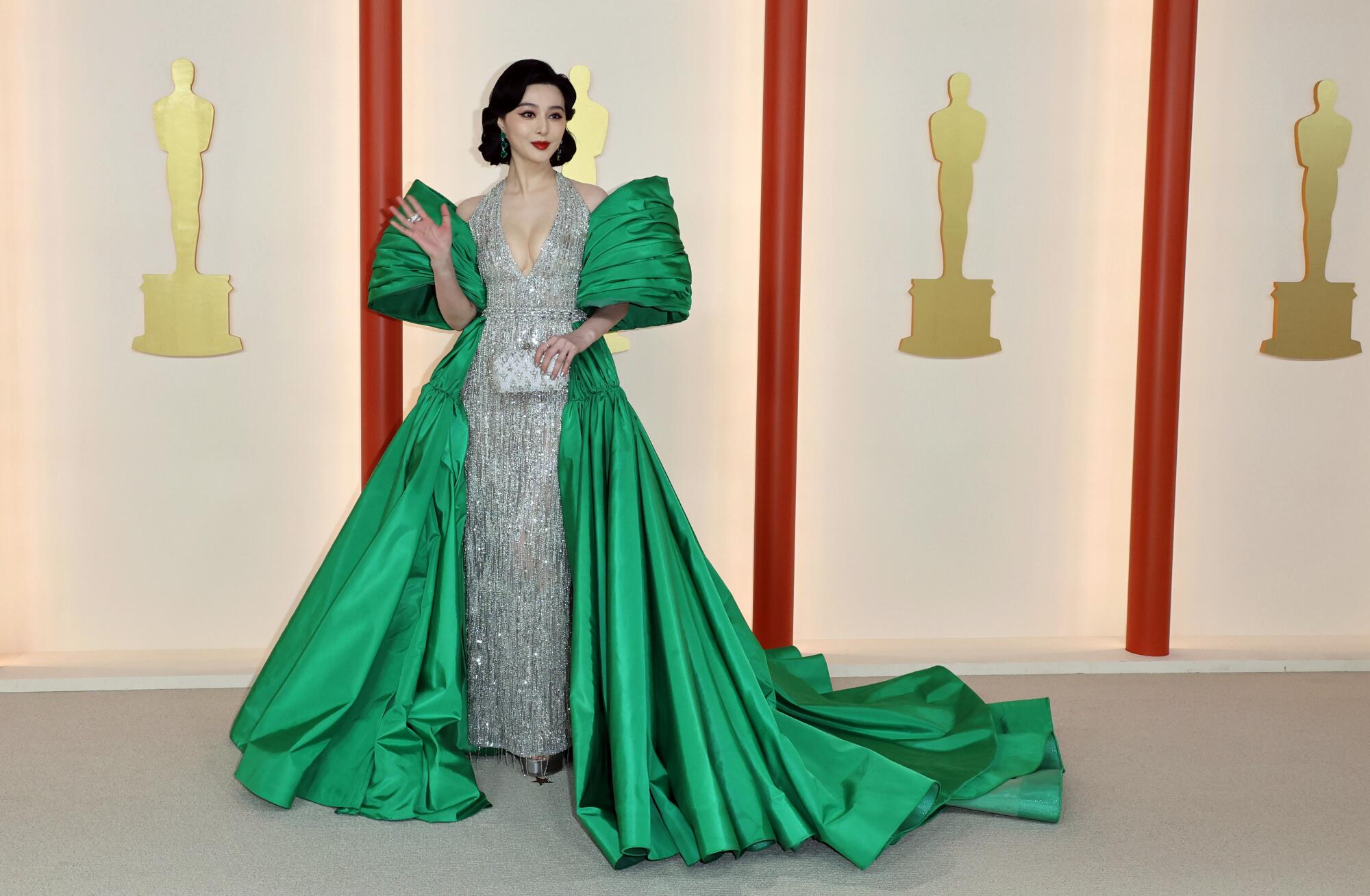 Fan Bingbing in a shimmering silver gown with green, cape-like sleeves and wrap-around, trailing green skirt. 