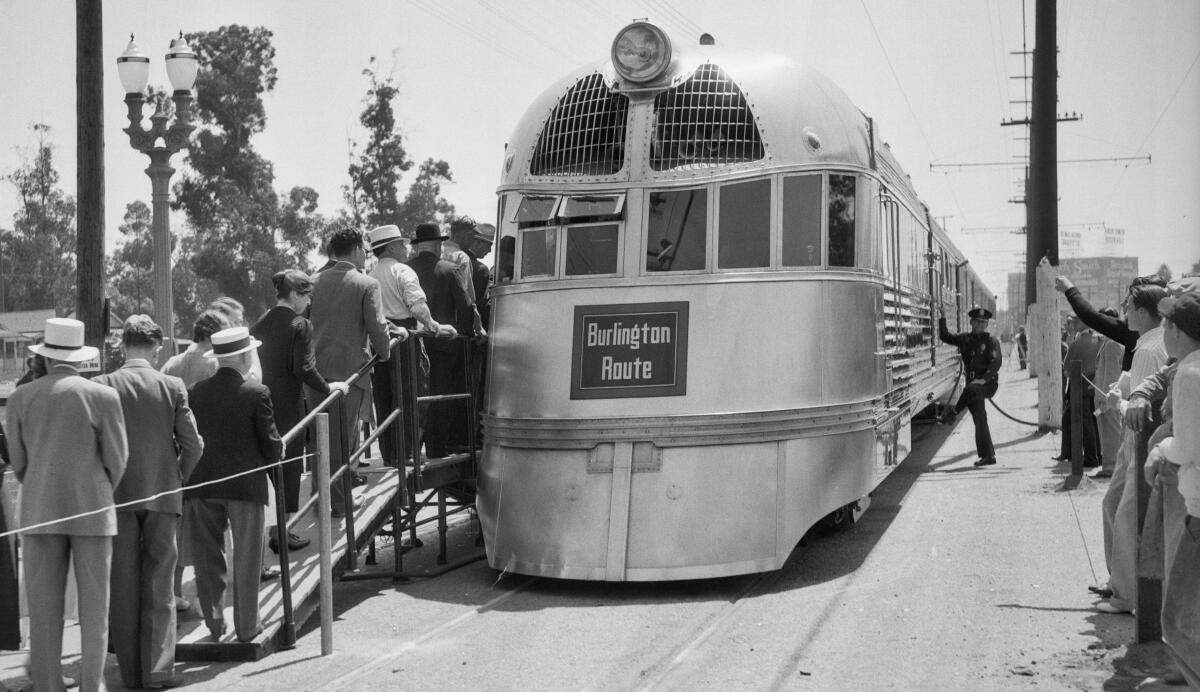 People stand in line to board a train.  The locomotive has a sign that says "Burlington Route."