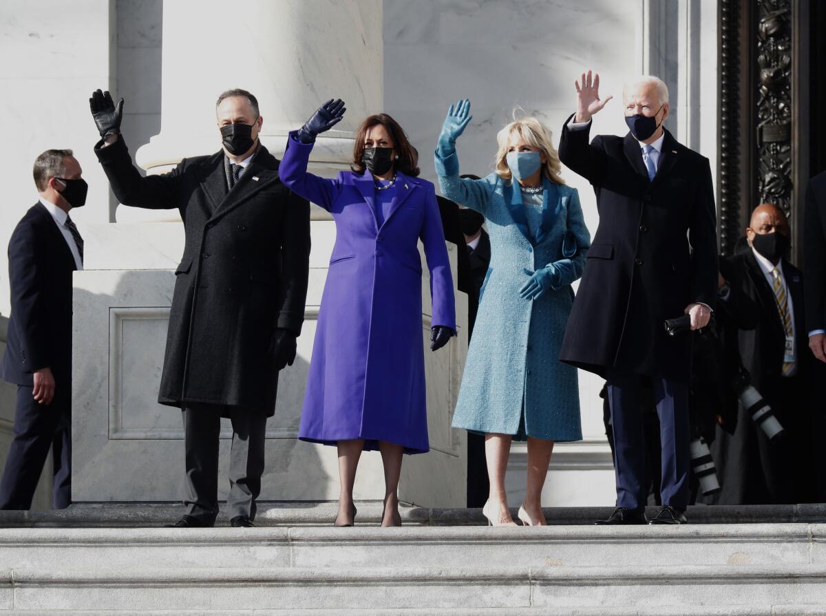 Douglas Emhoff in a black coat, Kamala Harris in purple, Jill Biden in blue and Joe Biden in black wave to the crowd. 