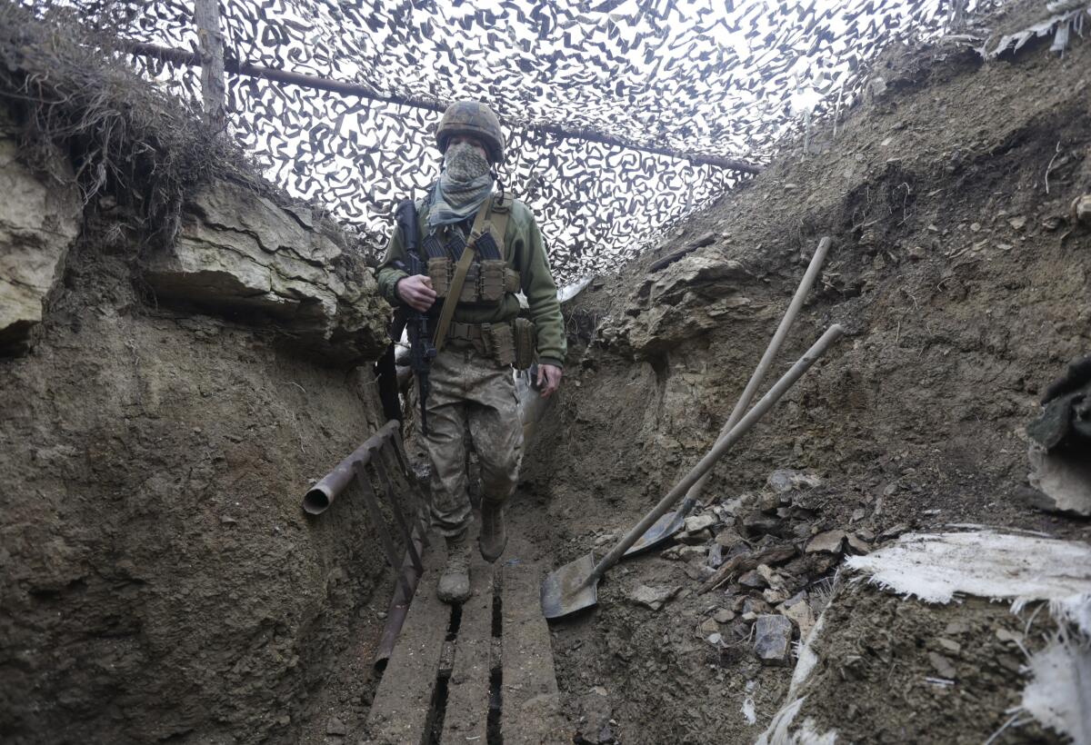 A Ukrainian solder walks in a trench under a camouflage net.
