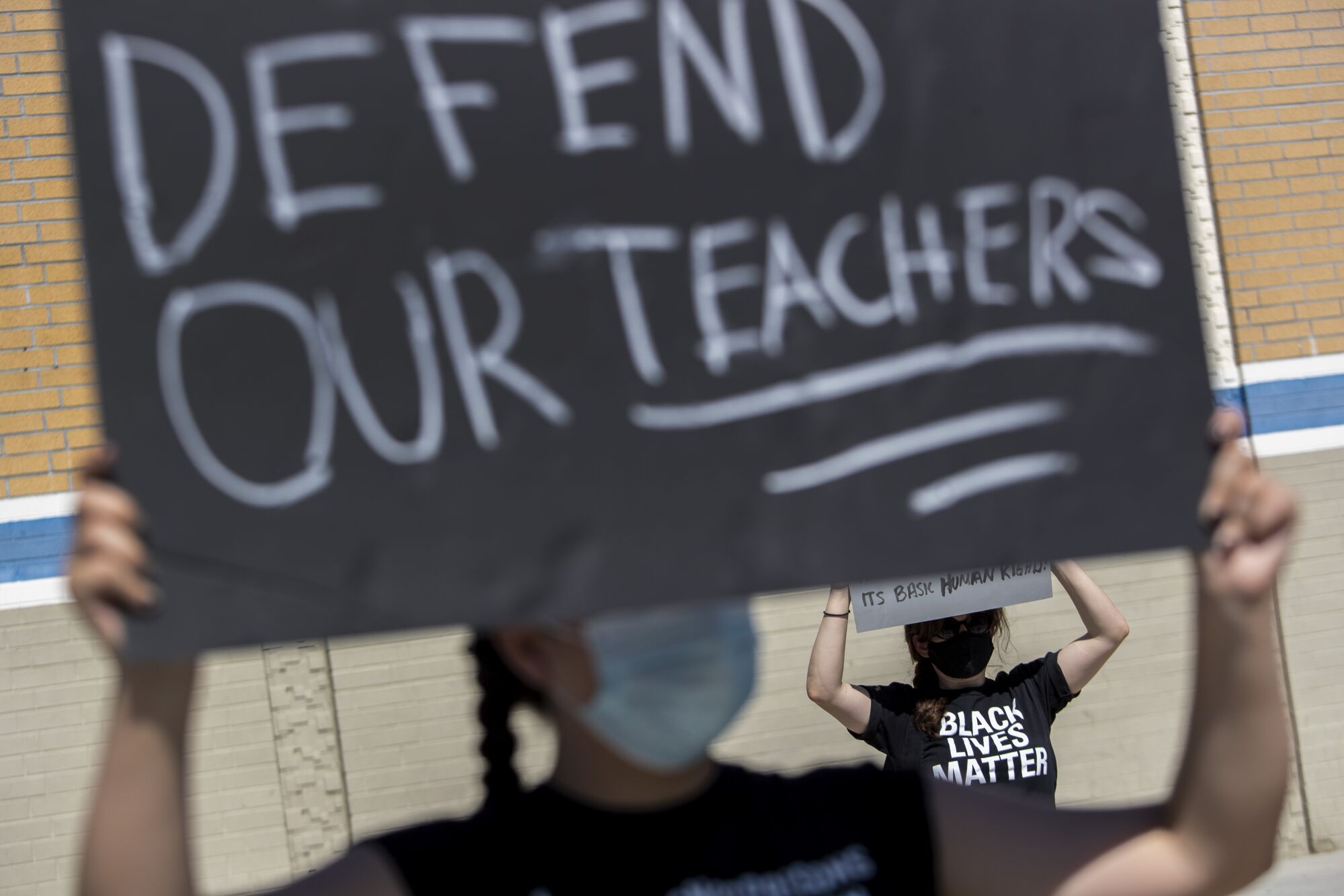 A student holds a sign that says "Defend our teachers" at a protest supporting a teacher who wore an "I can't breathe" shirt