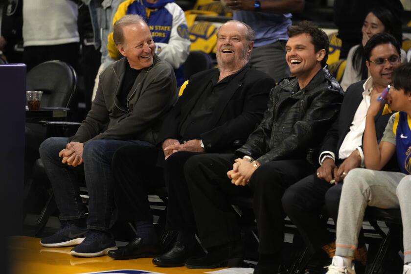 Jack Nicholson in black suit, sitting court side at Lakers Game, smiling alongside other members of the crowd