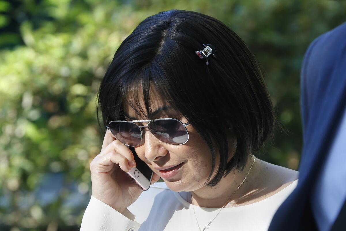 A woman wearing sunglasses holds a cellphone against her right ear outdoors.