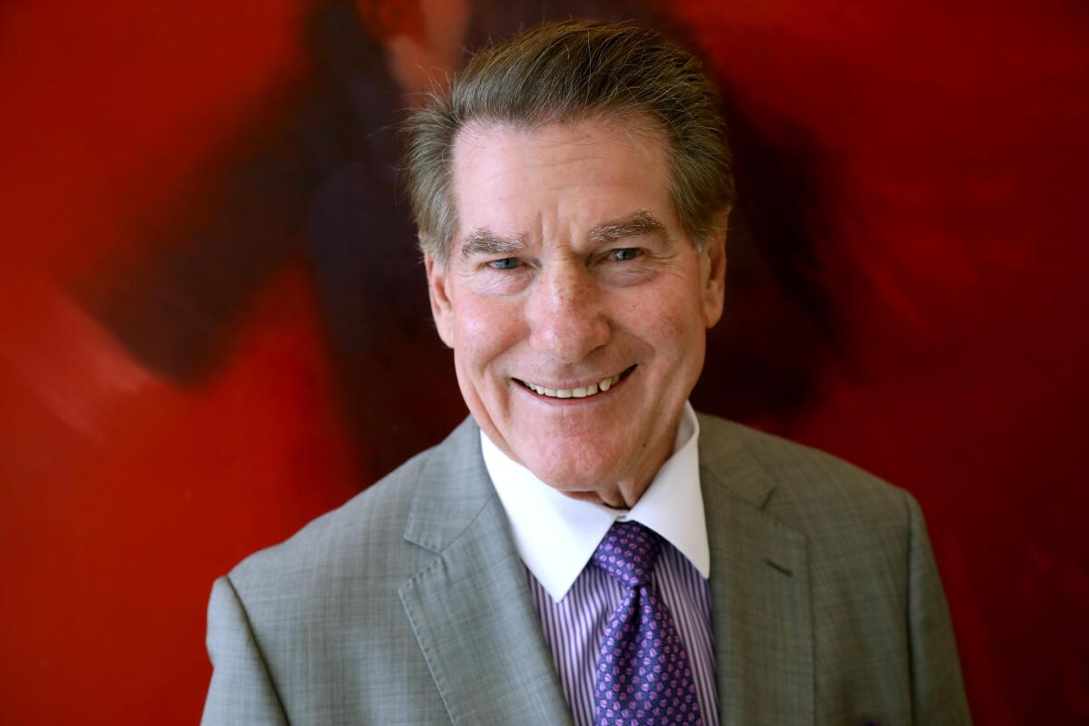 A smiling man with dark hair, in gray suit and purple tie 