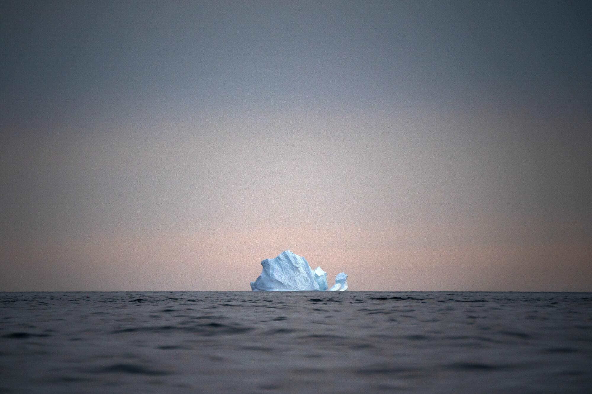 The sun sets over a large floating iceberg.