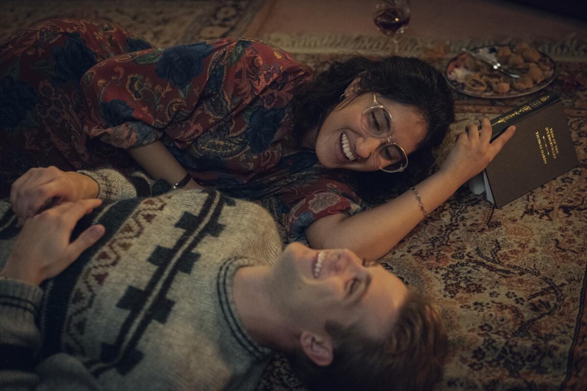 A man and a woman laying on a carpet reading and laughing.