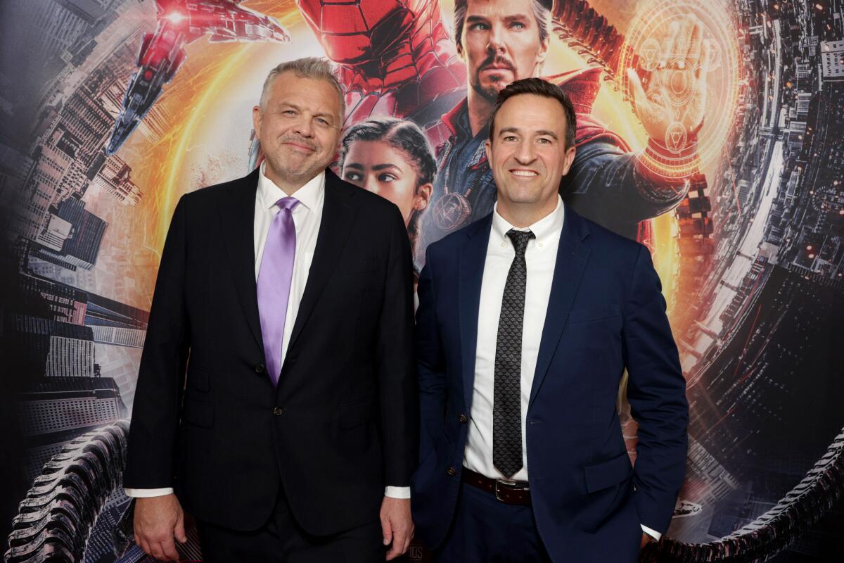 Two men in suits smile at the camera.