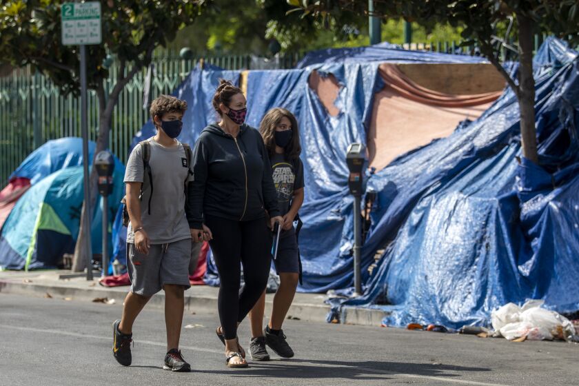 LOS ANGELES, CA - AUGUST 30: Sarah Tindall, middle, walks her son's Dylan and River past a homeless encampment near Larchmont Charter School - Selma located in the Hollywood neighborhood on Monday, Aug. 30, 2021 in Los Angeles, CA. Protesters got into a scuffle with Joe Buscaino aids at an event in Hollywood last month after the aide grabbed a sign from a protester near the encampment. (Francine Orr / Los Angeles Times)