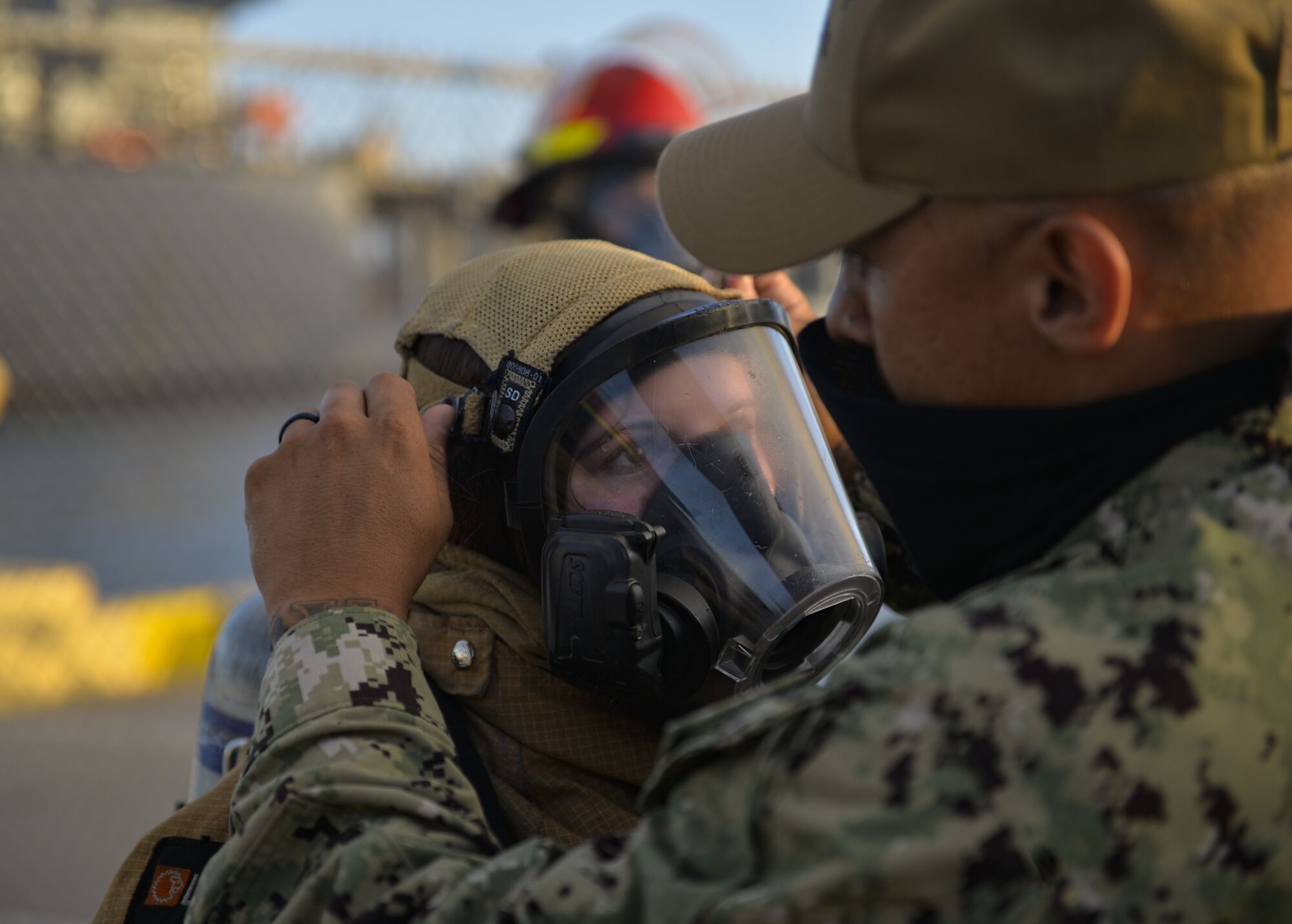 A U.S. Navy sailor is assisted in putting on her firefighting ensemble