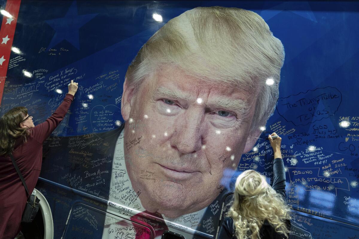 Trump supporters sign a campaign bus featuring a large image of the former president's face.