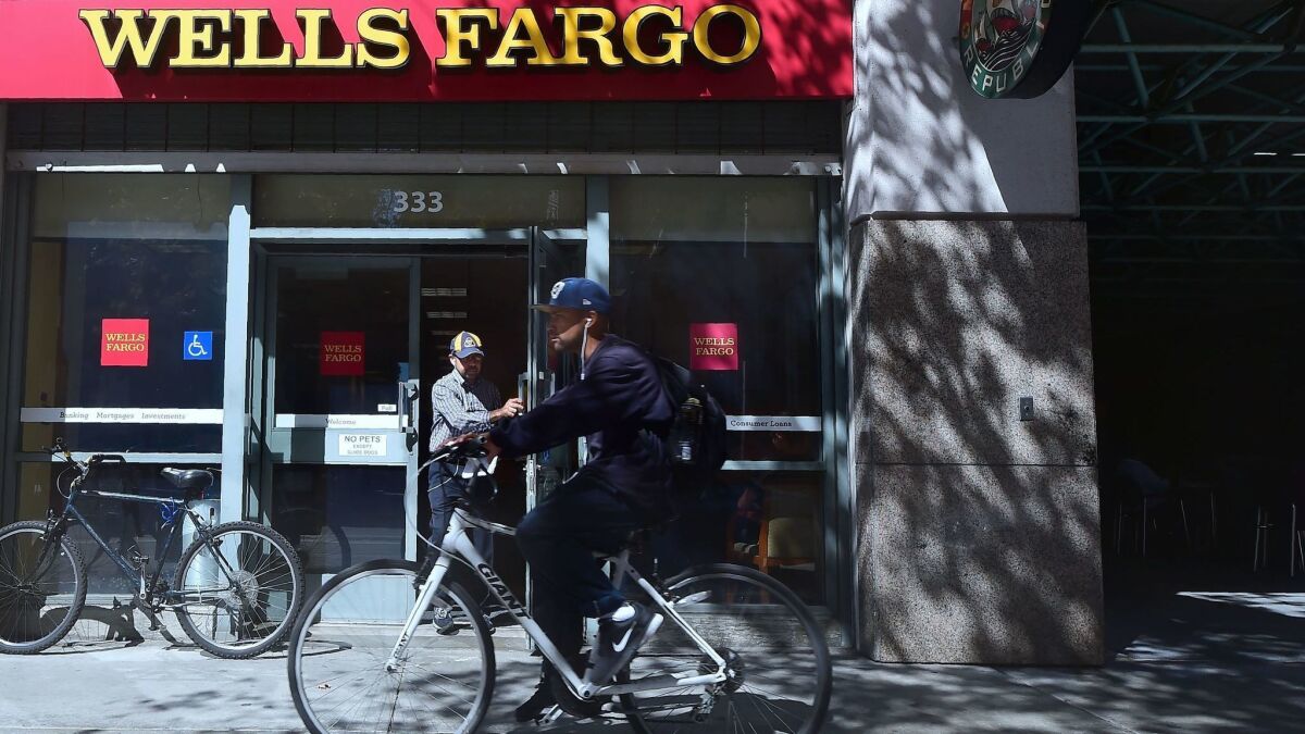 A man rides by a branch of Wells Fargo bank in Los Angeles in October 2016. The city of Los Angeles is adopting new bank disclosure requirements prompted by Wells Fargo's accounts scandal.