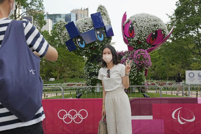A couple take a photo of large topiary of Miraitowa, left, the official mascot.