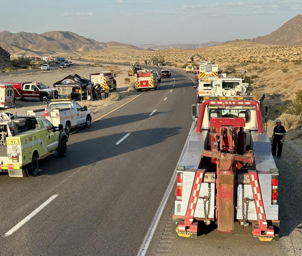 Emergency vehicles cast long shadows while parked on the shoulders of a desert highway
