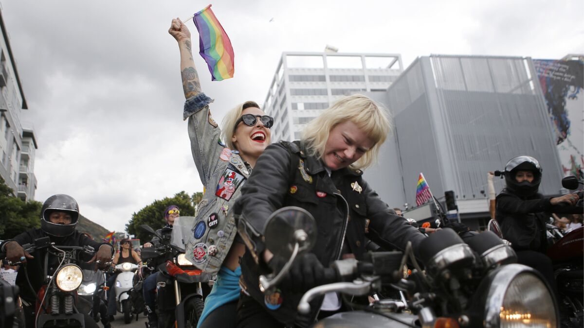 Kristen Wright, 36, thrusts a gay pride flag into the sky as Ashley Boyd, 30, rides a motorcycle on the parade route.