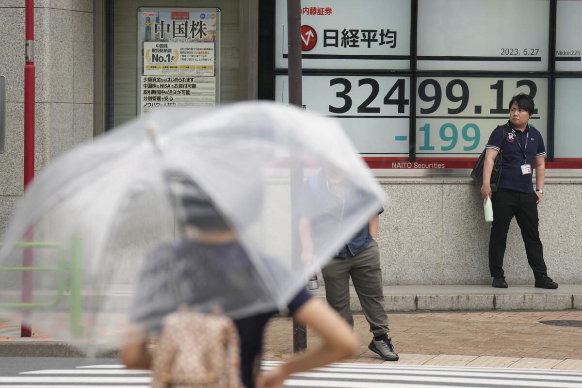 A pedestrian in Tokyo checks the latest Nikkei 225 numbers, holding a transparent umbrella.