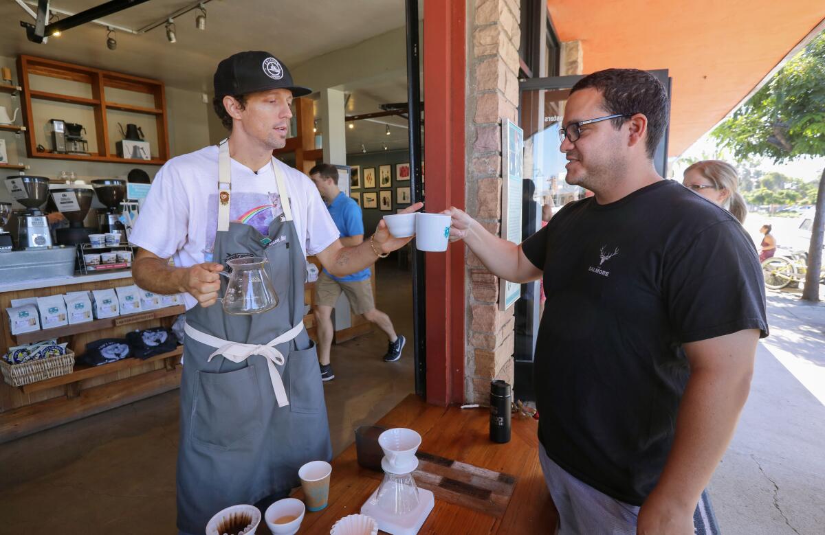 Singer-songwriter Jason Mraz toasts his new locally grown geisha coffee with customer Cory Suarez at Bird Rock Coffee Roasters in La Jolla. Mraz prepared the pour-over for the $35 cup of coffee.