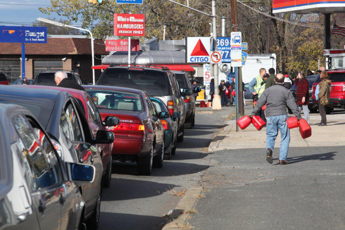 A motorist carries gas cans past a line of cars waiting for gas at a Citgo station in Hackensack, N.J.