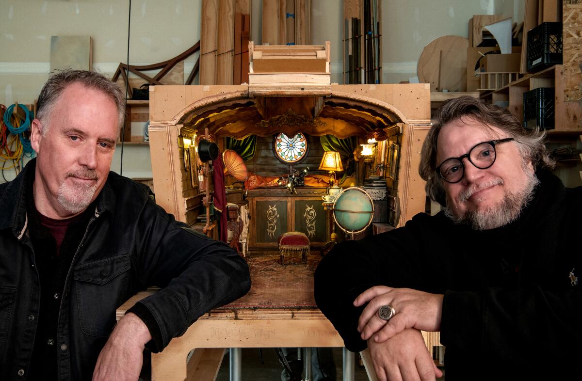Two men sit in front of a stop-motion model.