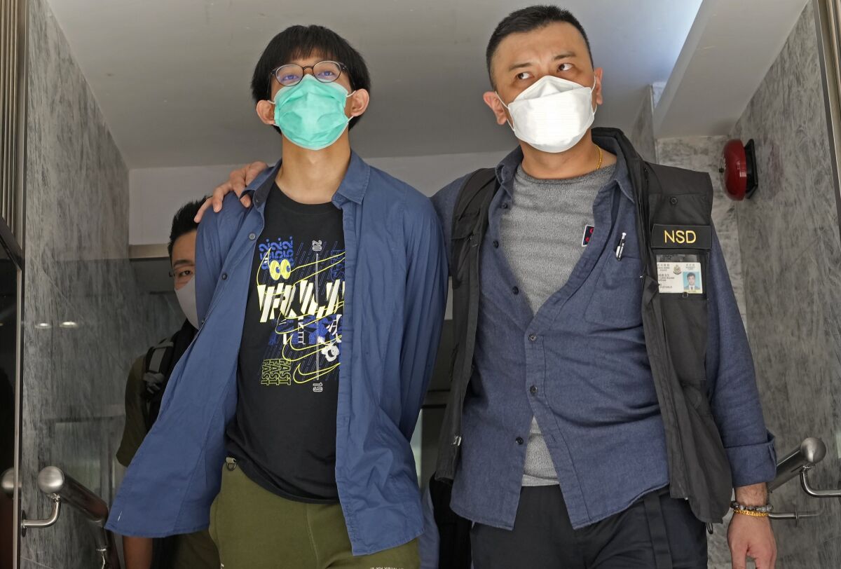 A student of Hong Kong University, left, is escorted by police officers after a home search in Hong Kong Wednesday, Aug. 18, 2021. Four members of a Hong Kong university student union were arrested Wednesday on accusations of advocating terrorism when they paid tribute to an attacker who stabbed a police officer and then killed himself, police said. (AP Photo/Vincent Yu)