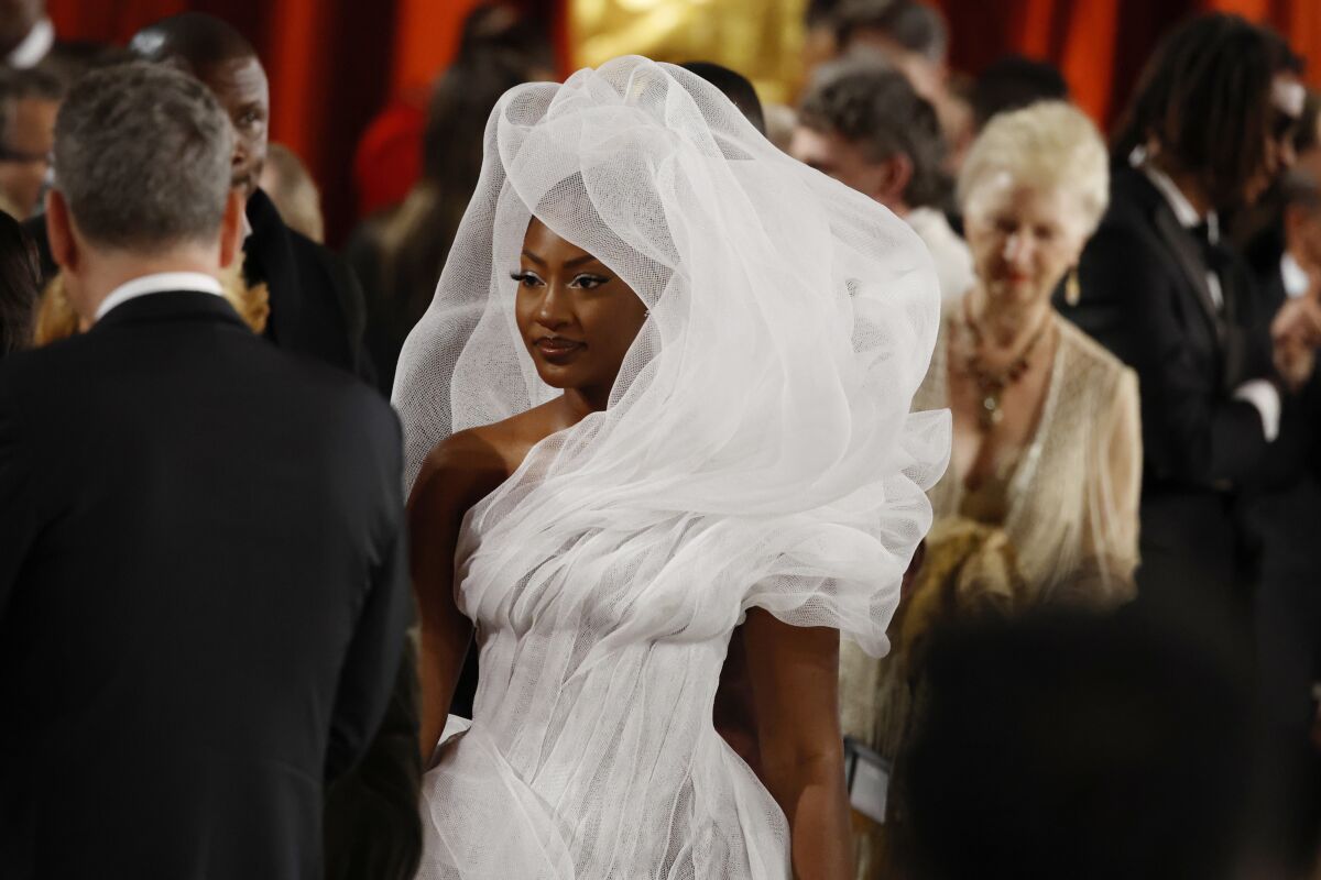 A woman wears a structural white gown that swirls a large could of fabric around her head.