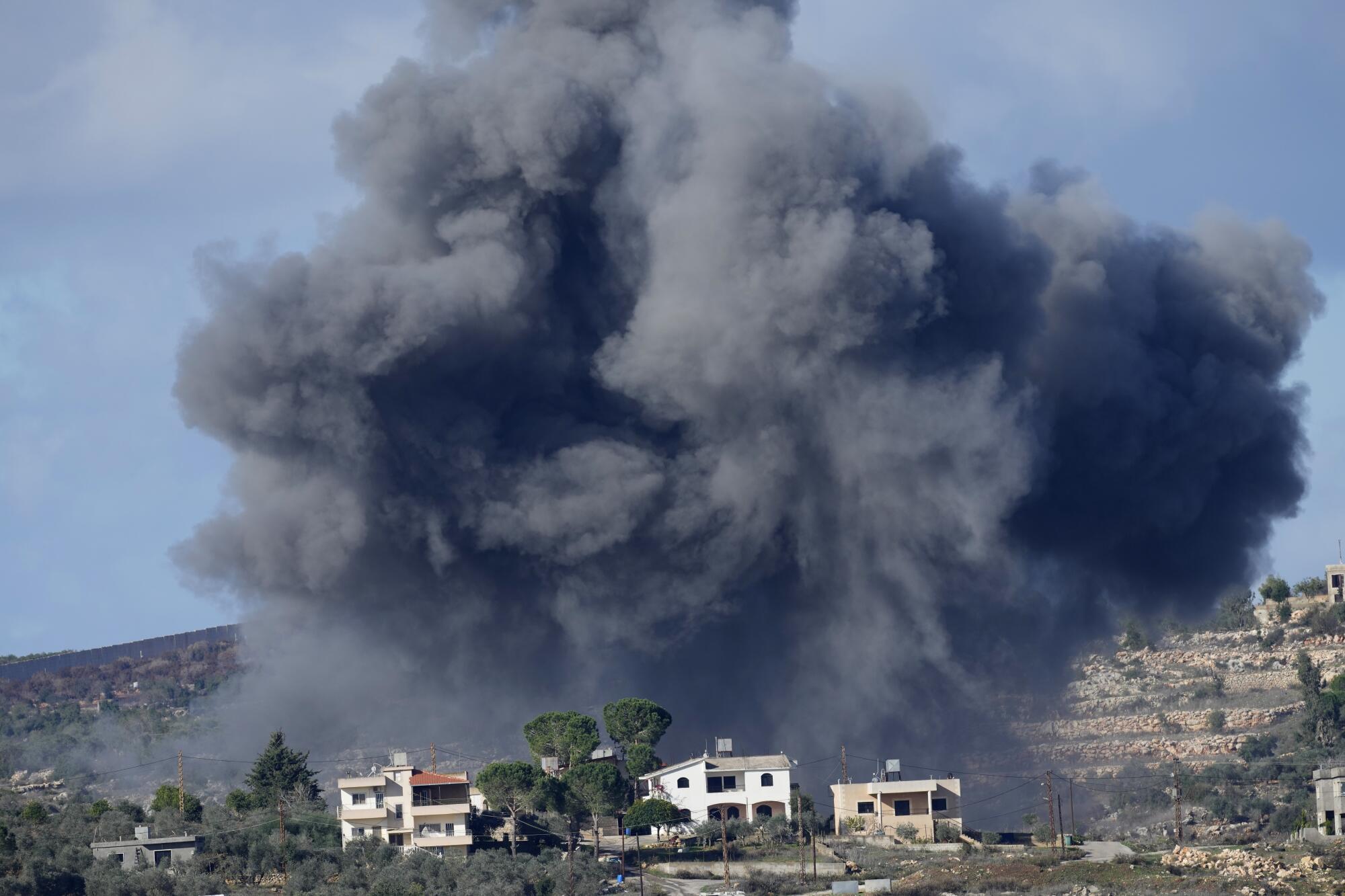 Huge clouds of black smoke rise above the buildings.