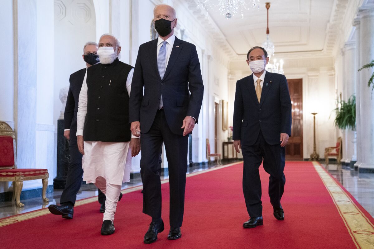 Four people in masks walking across a red carpet at the White House