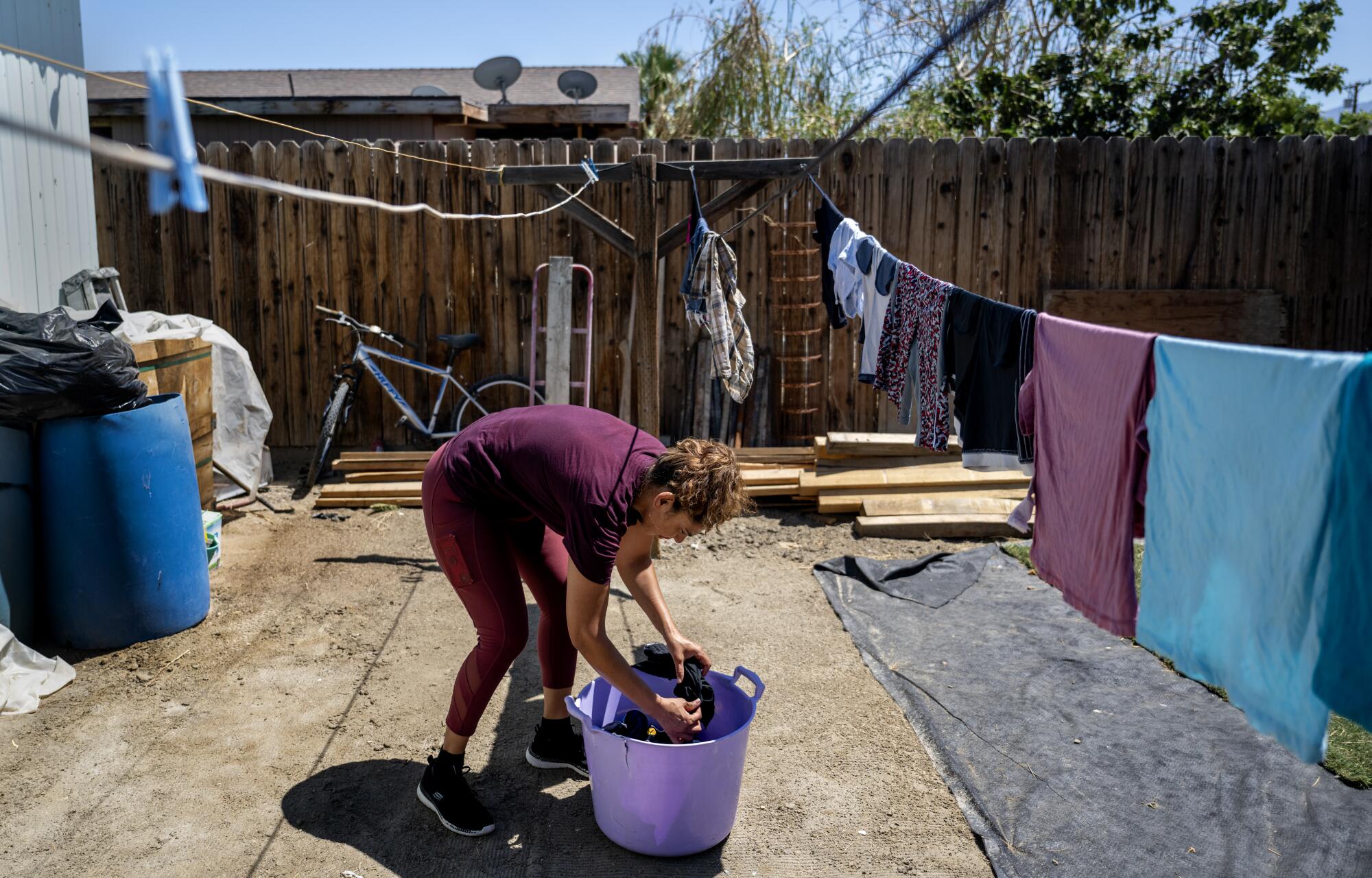 A woman takes laundry out of a bucket to hang on a line outside her trailer. 