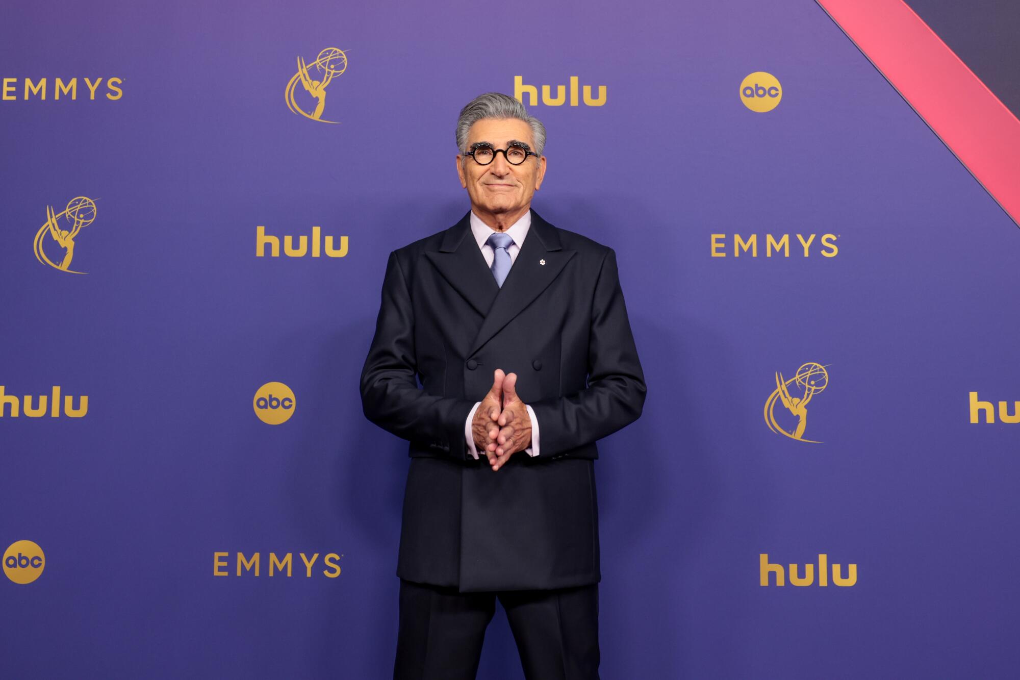 Eugene Levy wears a blue suit and tie.