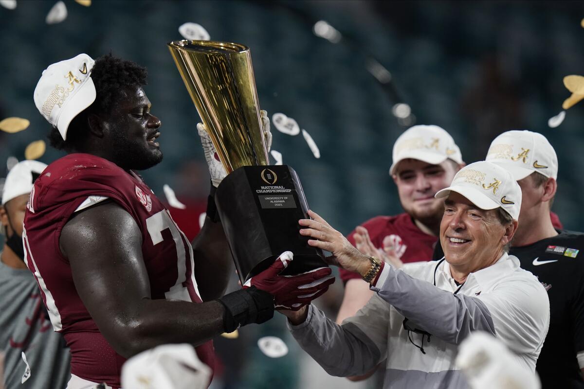 Alabama head coach Nick Saban and offensive lineman Alex Leatherwood hold the trophy 