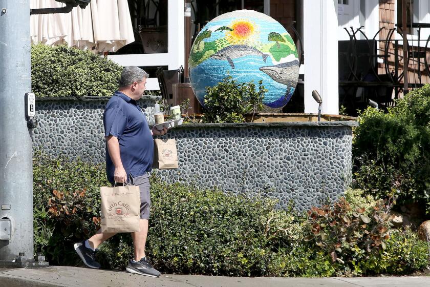 A patron of the Urth Cafe in Laguna Beach carries take-out as local businesses and restaurants are being asked to avoid small gathering and uphold social distances during the widening Coronavirus pandemic.