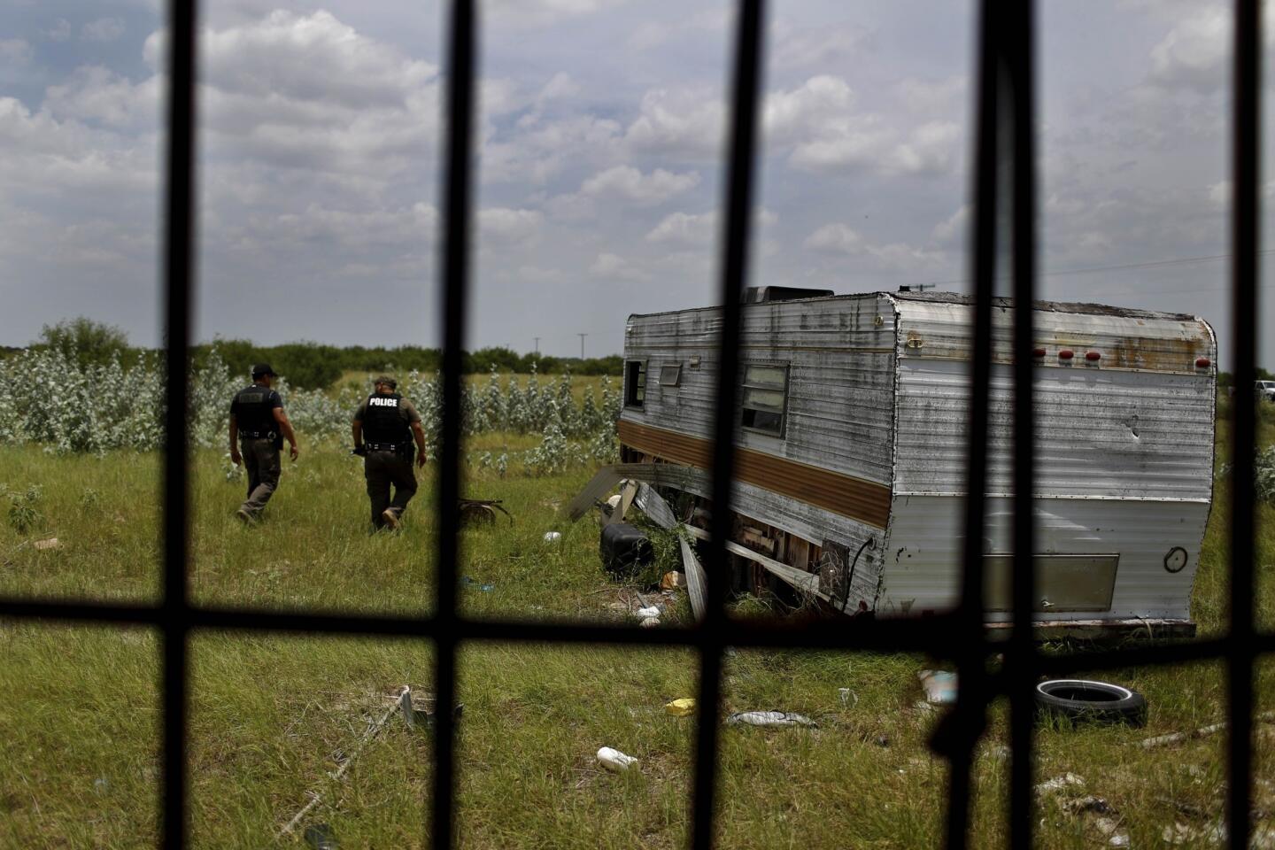 Deputies Domingo Aguirre, left, and Daniel Zamarripa, stand outside an abandoned trailer used by migrants for shelter on their journey north through Texas' Brooks County.