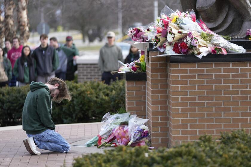A student kneels where flowers are being left at the Spartan Statue on the grounds of Michigan State University, in East Lansing, Mich., Tuesday, Feb. 14, 2023. A gunman killed several people and wounded others at Michigan State University. Police said early Tuesday that the shooter eventually killed himself. (AP Photo/Paul Sancya)