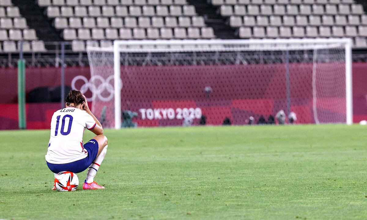 Carli Lloyd crouches on the soccer field, head in her hands, at the Tokyo Olympics.