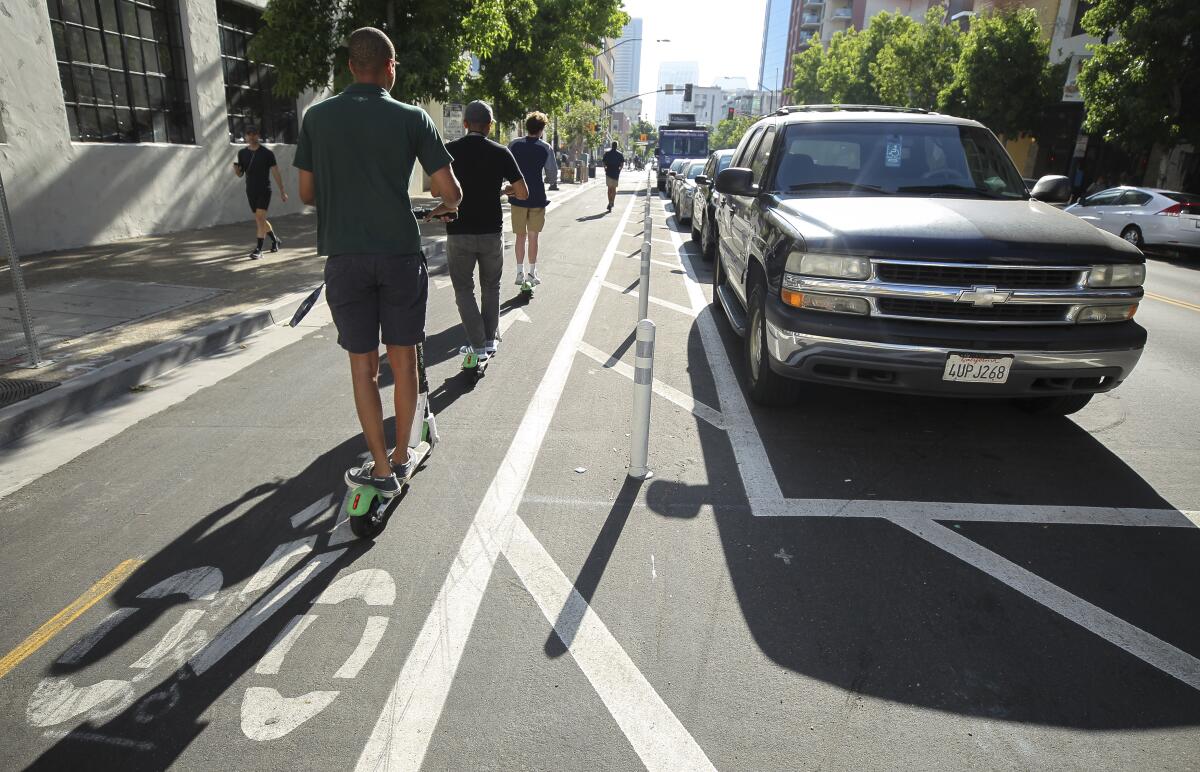 People ride electric scooters on a bike lane next to parked cars