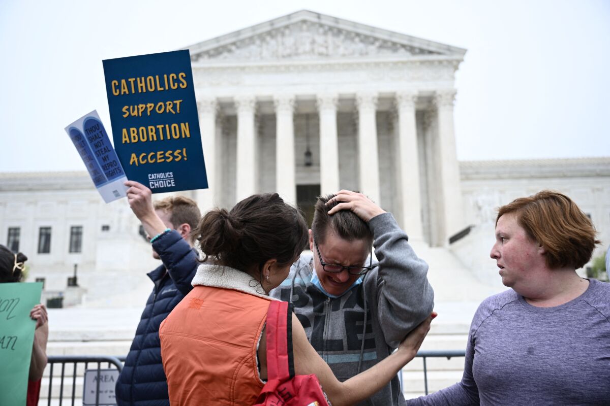 A woman consoles a person crying, as a man, left, holds up a sign saying Catholics support abortion access. 