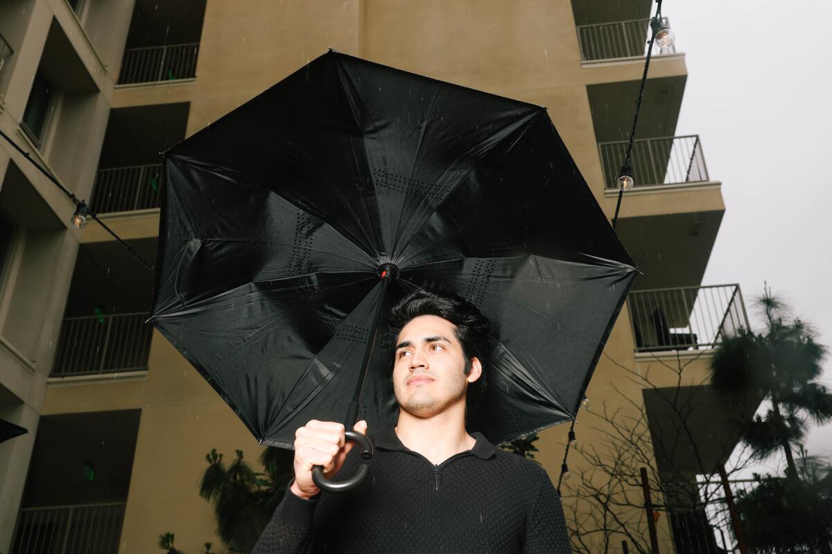 A man holding an umbrella outside of a beige apartment complex.